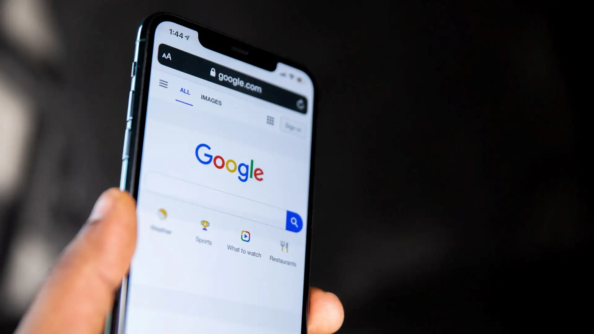 A person holding a phone with the Google search bar displayed.