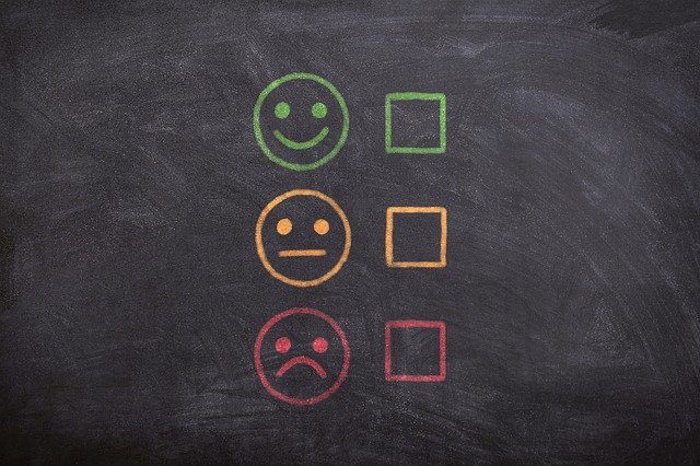 A smiley face, neutral face, and a sad face represented in green, yellow, and red colors on a blackboard